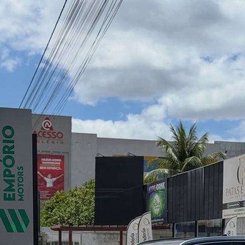 Vista da rua com a torre da Empório Motors à esquerda, prédios vizinhos, uma palmeira e céu com nuvens